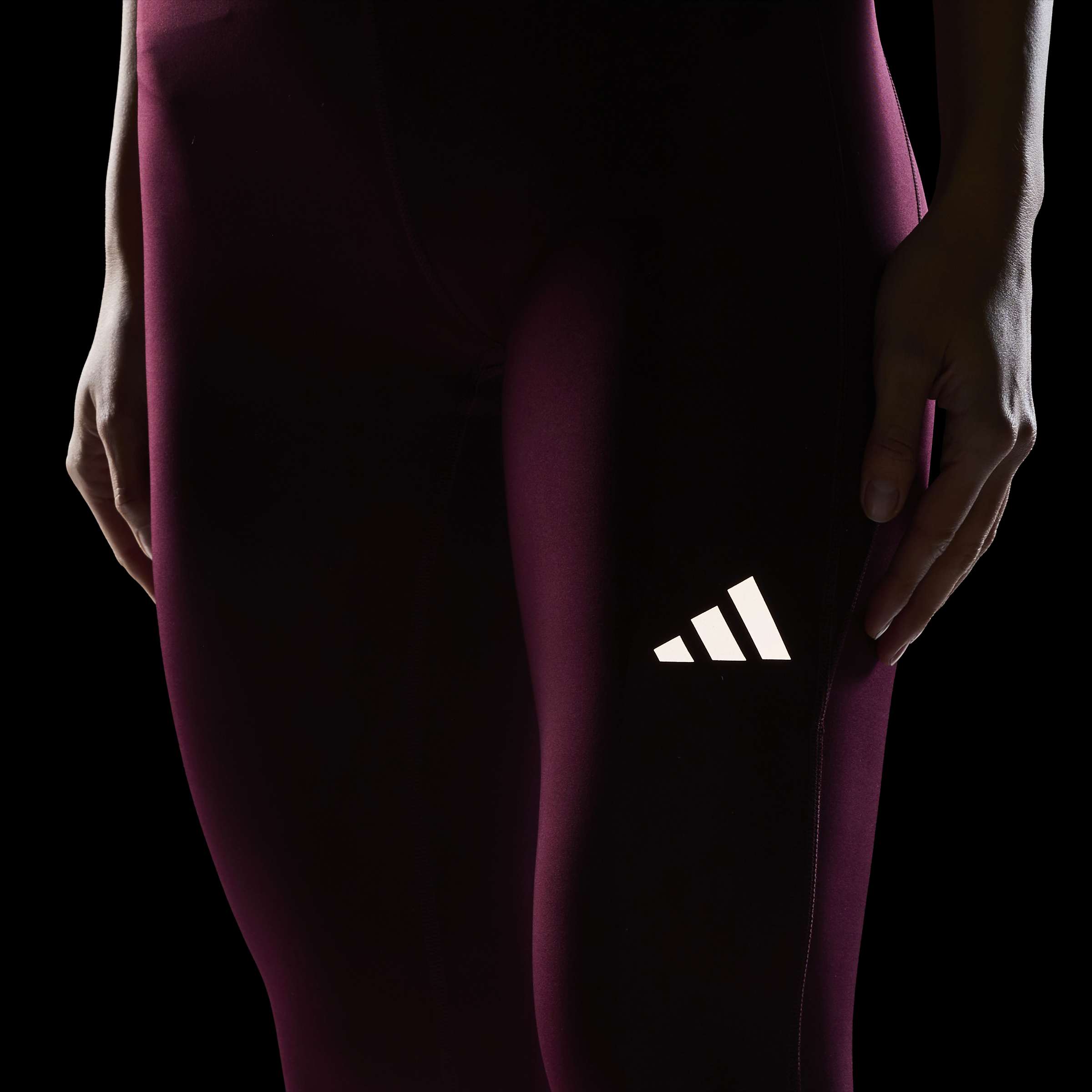 Дамски клин за бягане adidas Run Essentials – детайл на светлоотразителното лого adidas върху бордо материя на тъмен фон